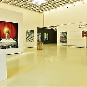 Innenraum der Galerie mit abstrakten Großbildern an den Wänden und Skulpturen auf weißen Sockeln. 