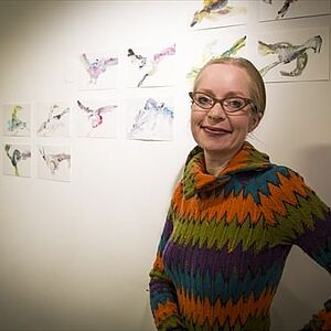 Die Künstlerin Mischka Reska steht vor einem Bild mit dem Titel "Vögel, Bären und andere Untiere".