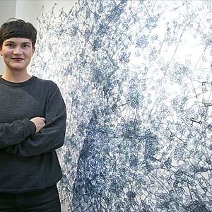 Rebekka Bauer steht neben ihrem Bild, das in blau-grau Tönen gehalten ist. 