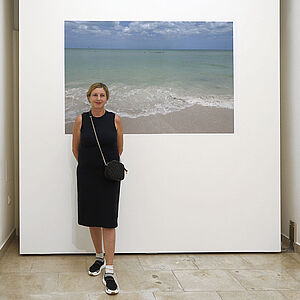 Foto mit Elisabeth Wörndl, dahinter ein Bild mit Strand und türkisblauem Meer