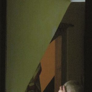 Fotografie eines Teilausschnittes eines Mansardenfensters an dem der beinahe kahlköpfiger Kopf eines Menschen im Profil zu sehen ist, der sich mit der rechten Hand Stirn und Augen bedeckt.