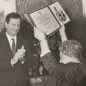 Schwarz-Weiß Foto von Fr. Dr. Firnberg, sie hält die Urkunde über ihren Kopf während Bürgermeister Reschen neben ihr applaudiert