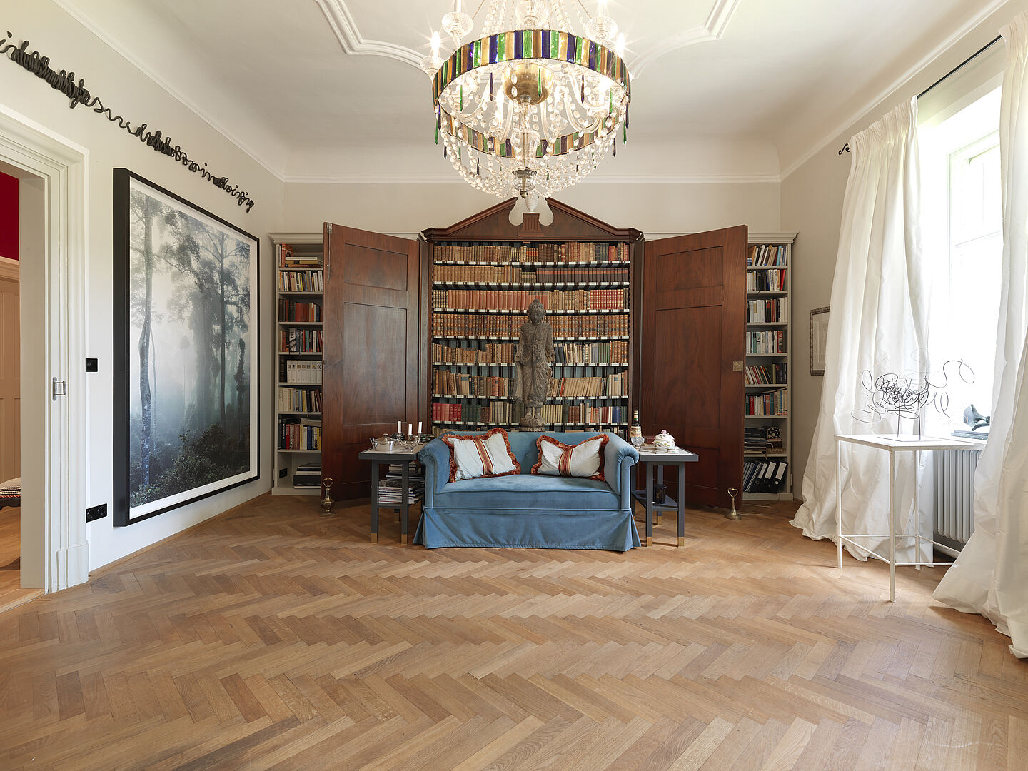 Foto eines Zimmers mit blauer Couch vor eine Bücherwand